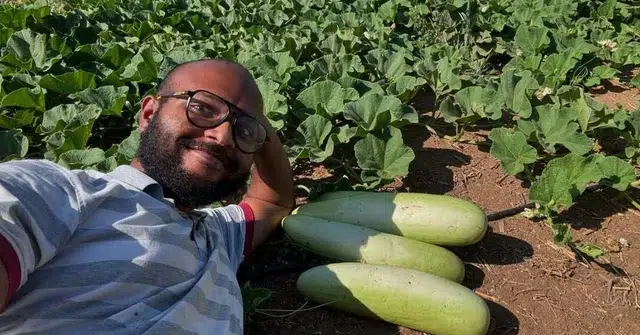 A smiling man takes a selfie in his farm field beside freshly harvested bottle gourds.