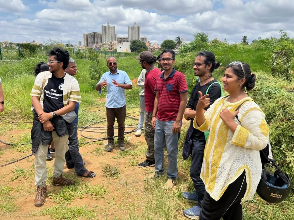 A group of people standing on a farm, smiling and talking as one man gestures during the discussion.