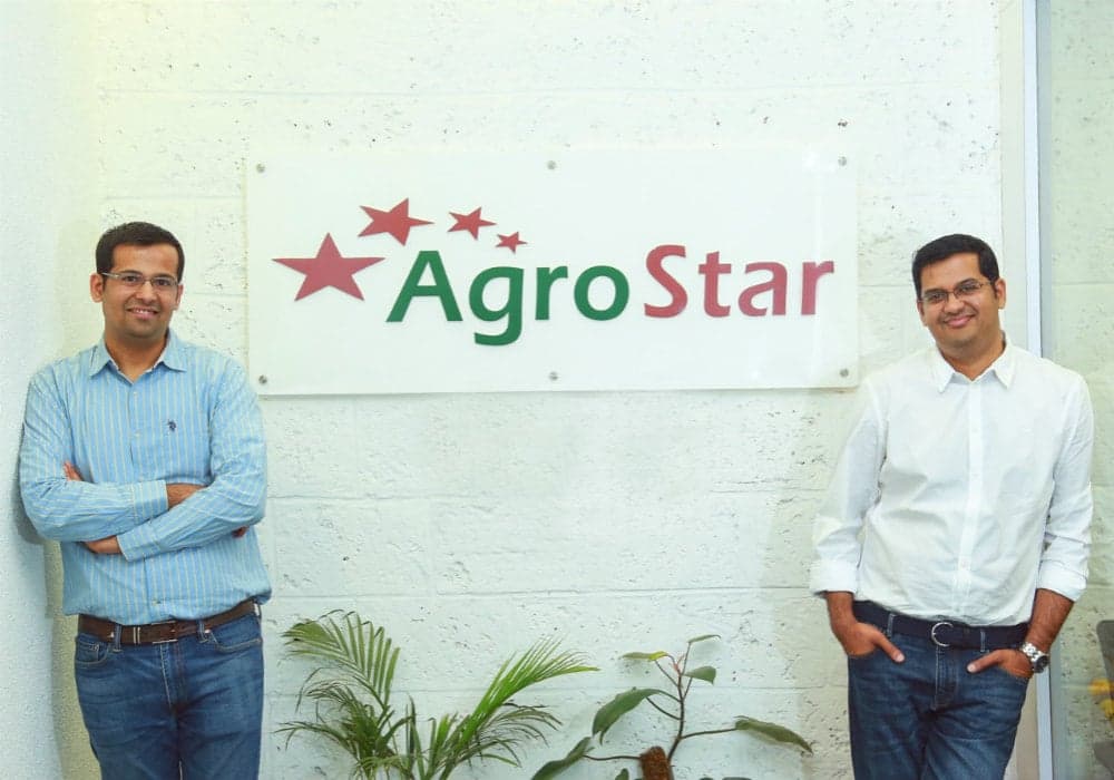 Two men standing beside a wall-mounted AgroStar signboard inside an office.